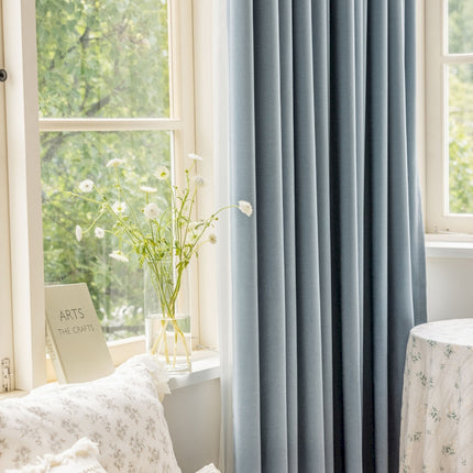 a window with a blue curtain and a white table with a vase of flowers