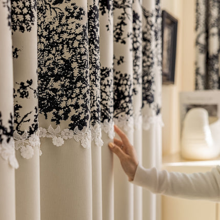 a woman standing next to a window covered in black and white curtains