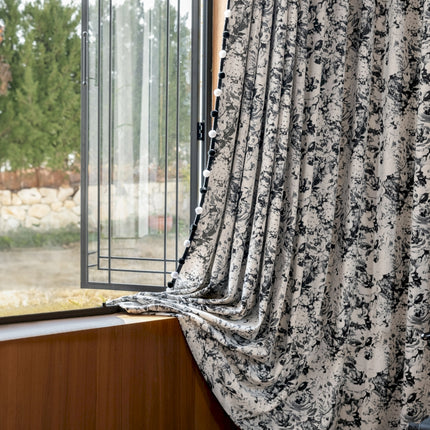 a window with a black and white flowered curtain
